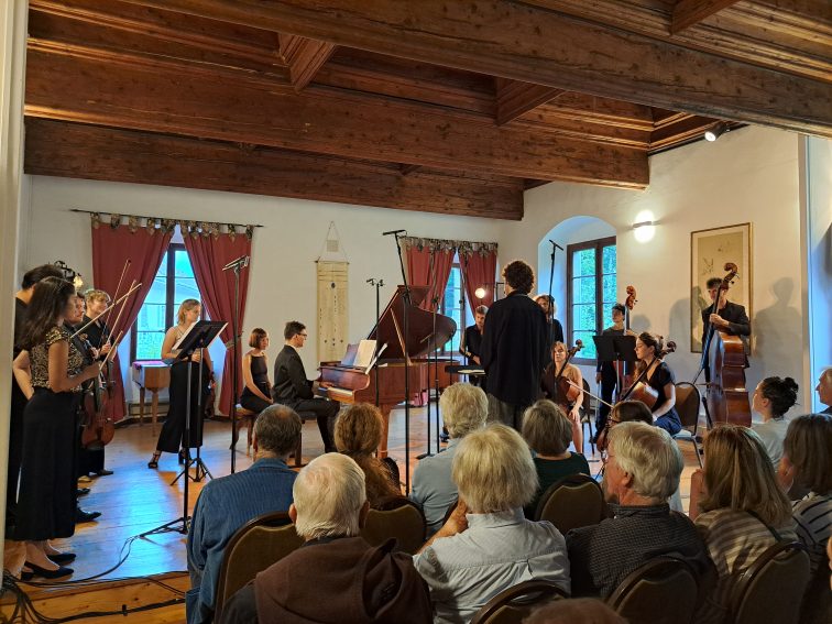 Musicians playing instruments inside the historic Priory in Talloires, with stone walls and wooden beams creating a cozy, musical atmosphere.